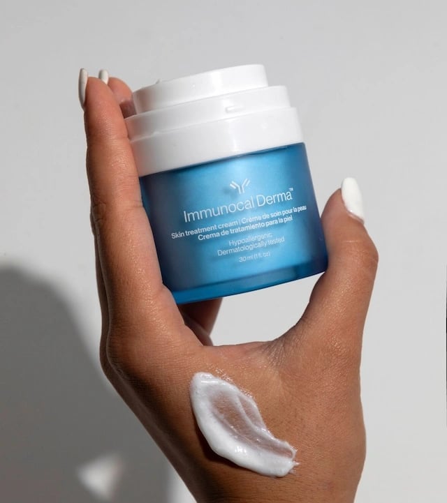 Mano sosteniendo frasco azul de Immunocal Derma con muestra de crema en la piel